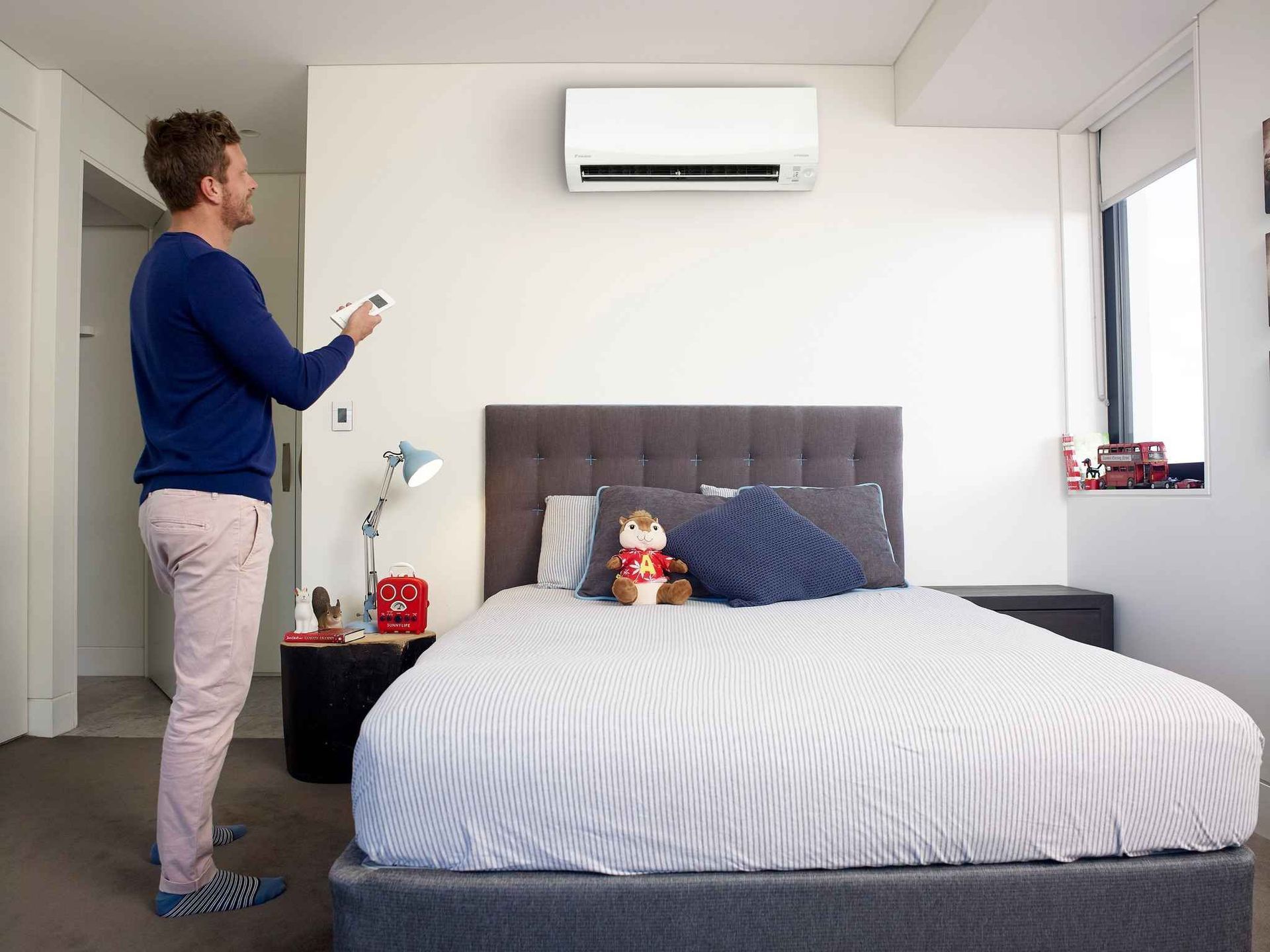 A Man Is Standing in A Bedroom Holding a Remote Control — McGuire Air & Refrigeration in Proserpine, QLD