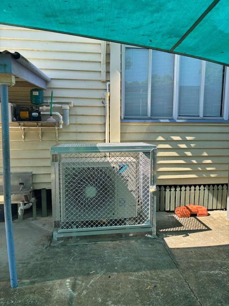 An Air Conditioner Is Sitting Under a Green Umbrella in Front of A House— McGuire Air & Refrigeration in Proserpine, QLD