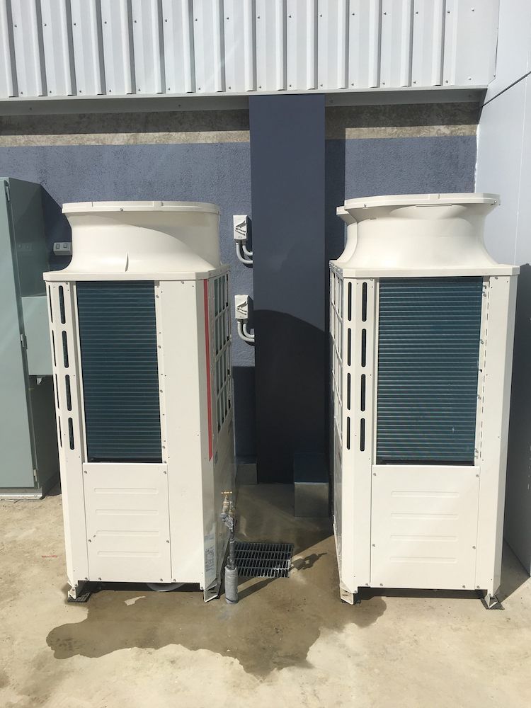 Two Air Conditioners Are Sitting Next to Each Other Outside of A Building — McGuire Air & Refrigeration In Sarina, QLD
