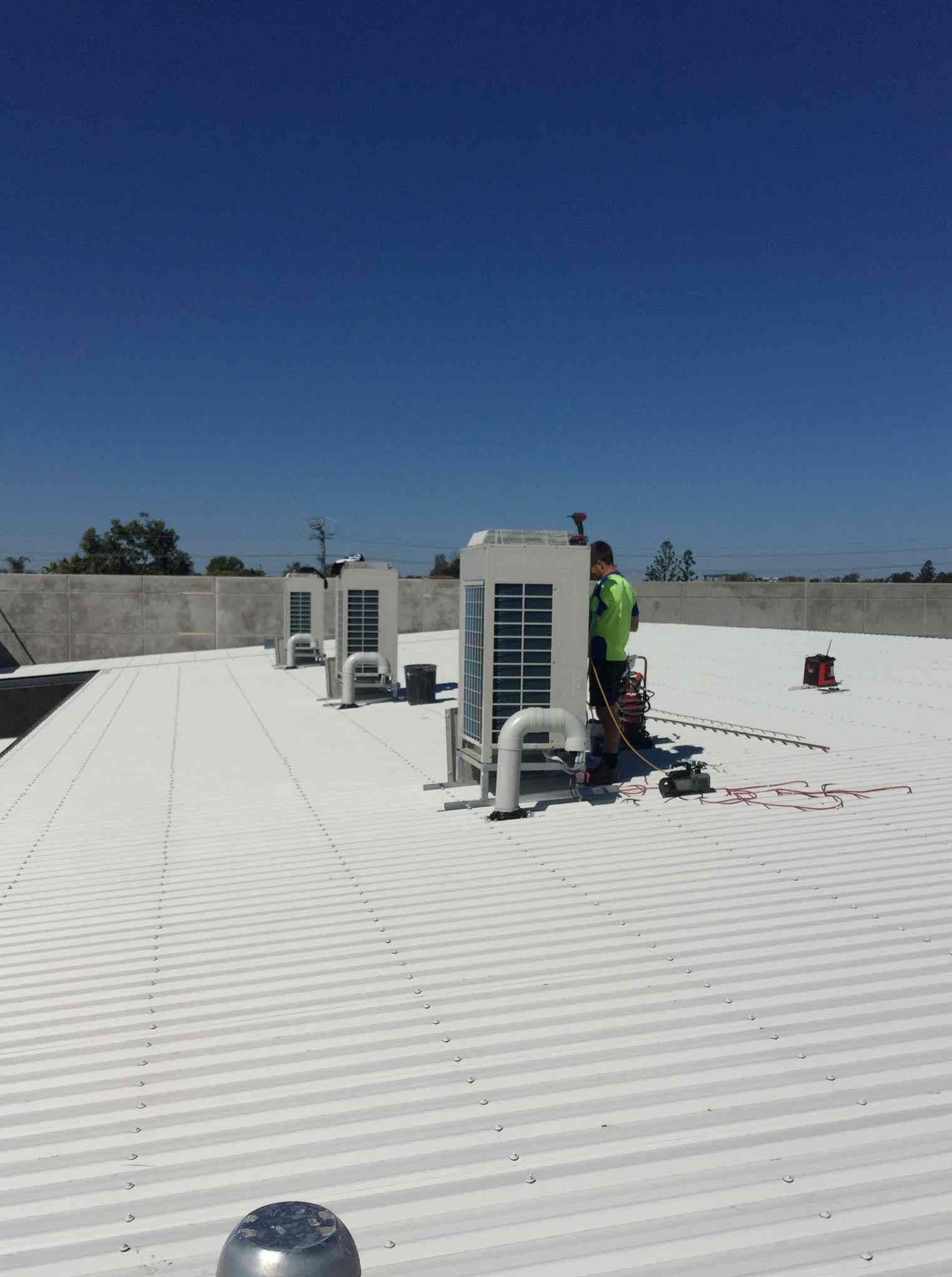 A Man Is Working on The Roof of A Building — McGuire Air & Refrigeration In Paget, QLD