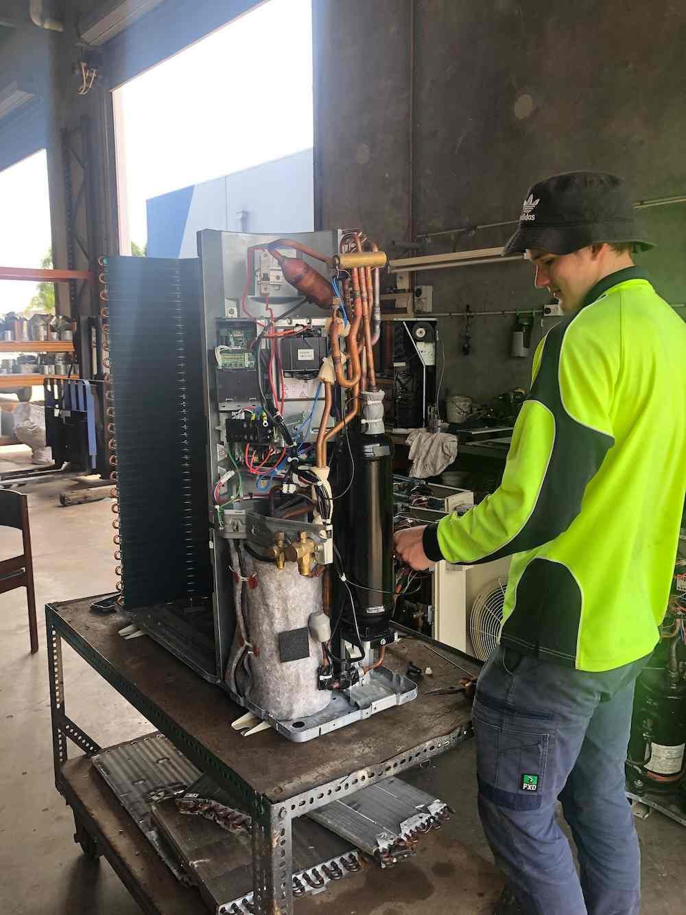 A Man Is Working on A Refrigerator in A Garage — McGuire Air & Refrigeration In Paget, QLD