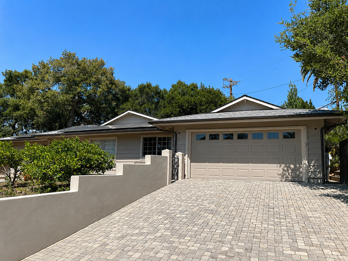 Single-story house with a brick driveway, cream exterior, and garage under a clear blue sky