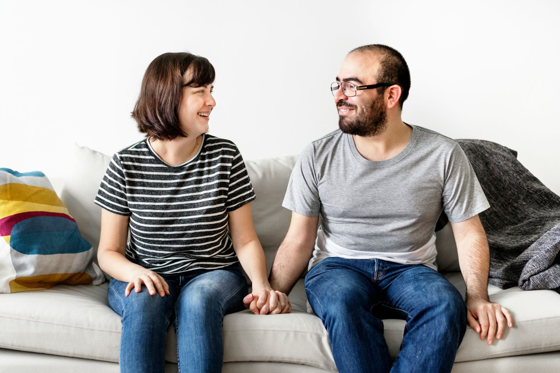 A couple sit on the couch about to engage in couples therapy that is polyam and kink-affirming. 