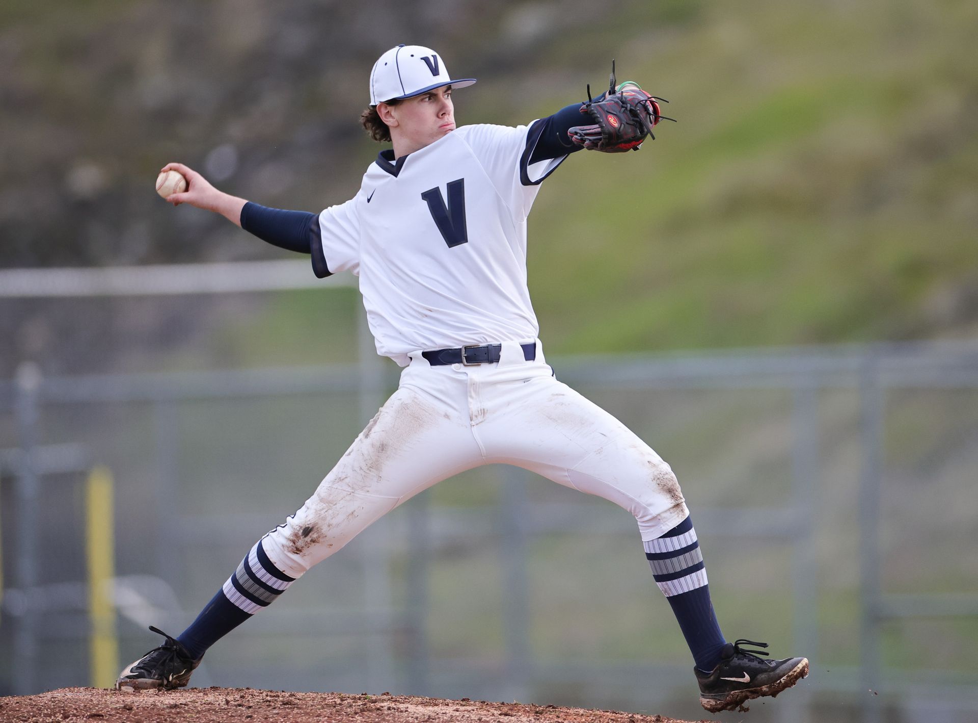 Baseball pitcher in white uniform winds up to throw a pitch on a field.
