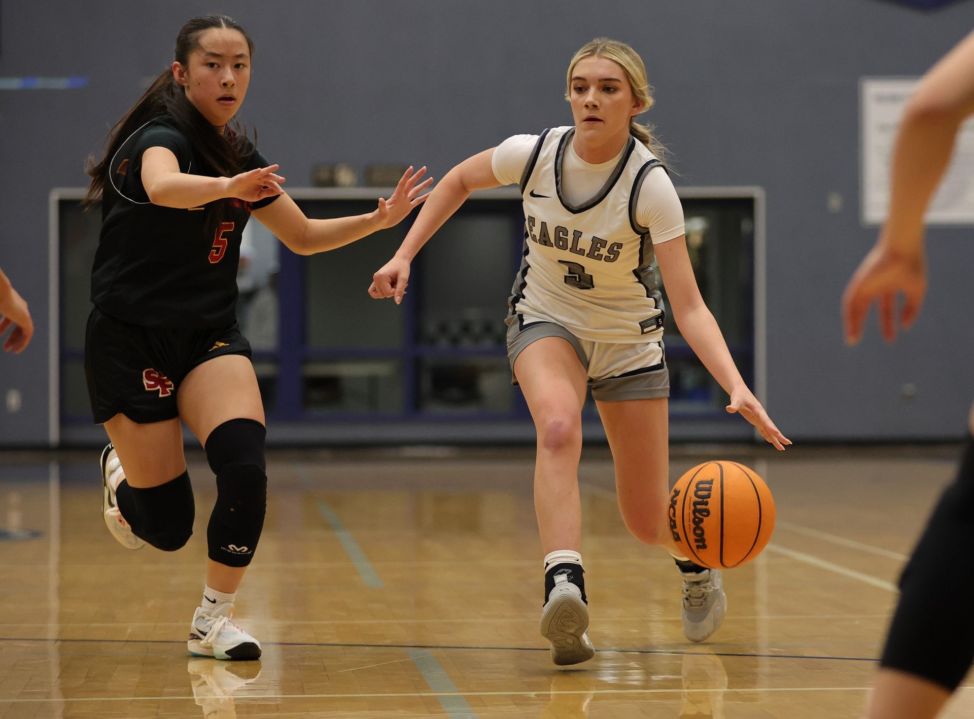 Basketball player dribbles ball, pursued by a defender on a court Vista Athletic Boosters