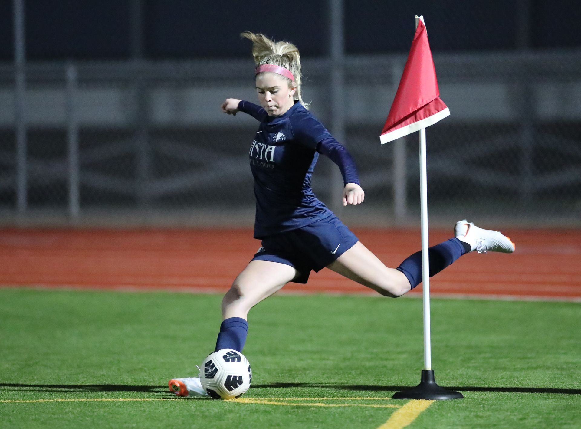 Soccer player in dark blue uniform kicks the ball near a corner flag on a green field.