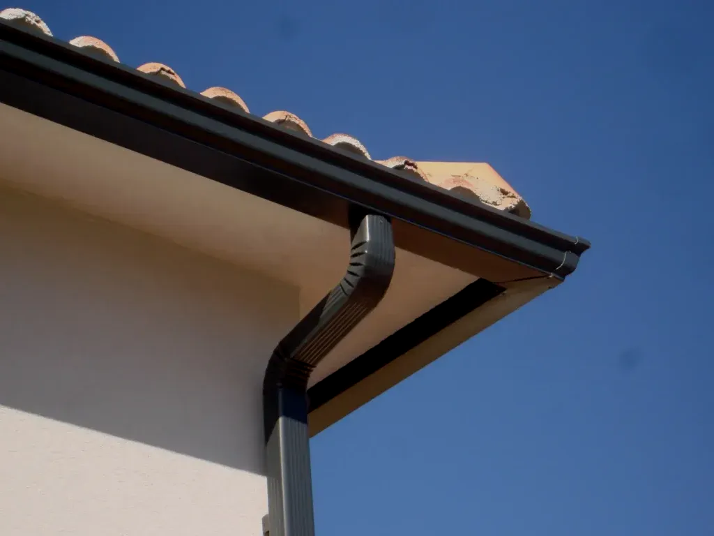 Gouttières et descentes pluviales noires sur une maison en stuc beige avec un toit de tuiles en terre cuite