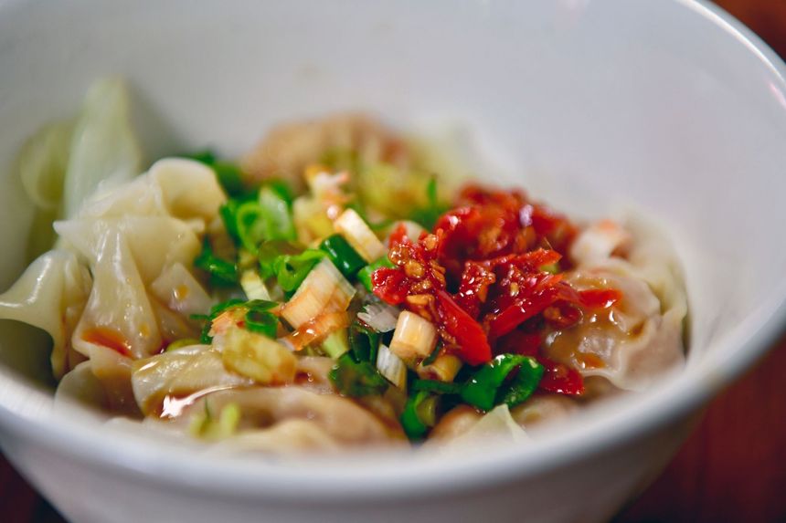 Bowl of dumplings topped with chopped green onions, red chili paste, and sauce