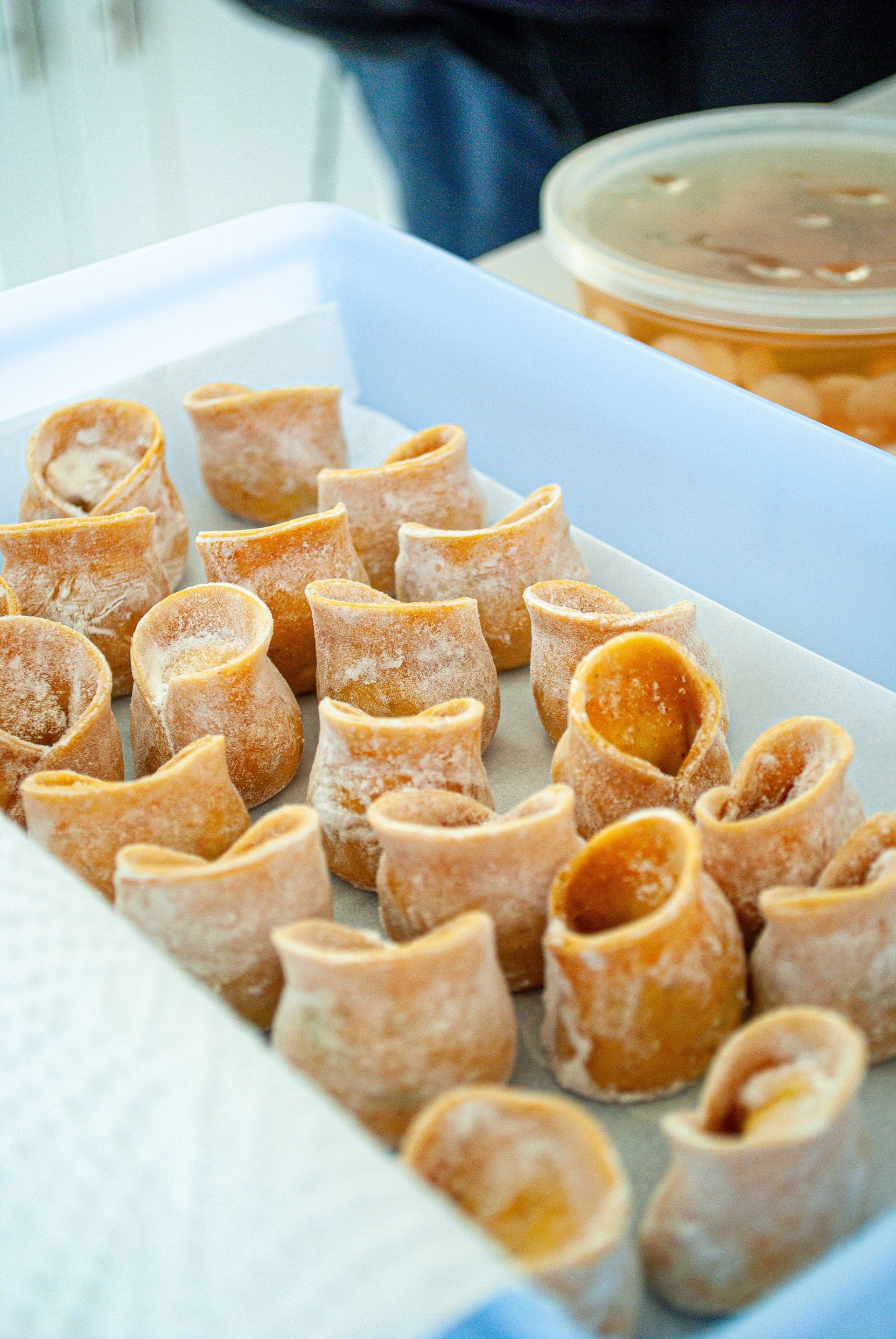 Tray of rolled pastries or wafers in a white container, with a cup of sauce in the background