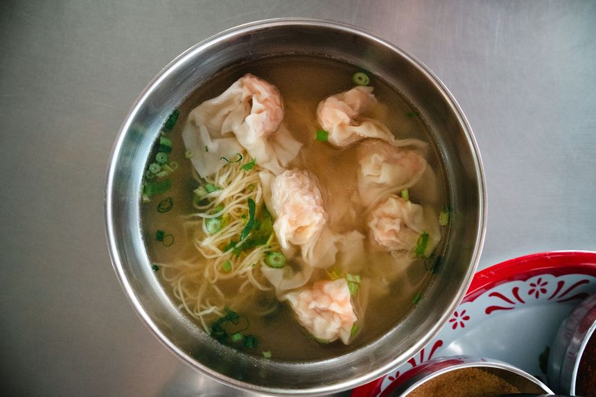 Bowl of soup with dumplings, noodles, and green onions on a table