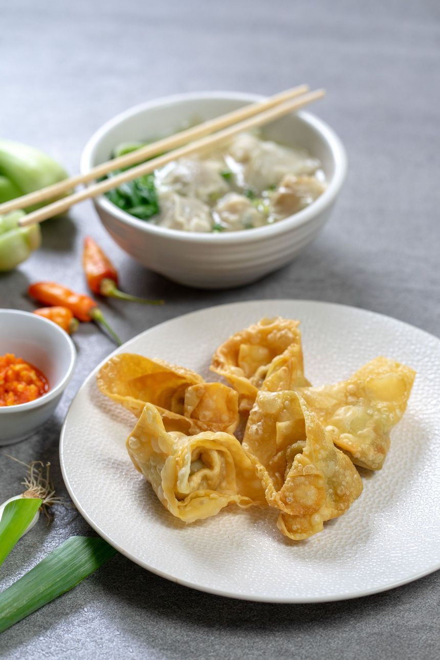 Plate of golden fried dumplings with chopsticks, served beside a bowl of dipping sauce and chilies