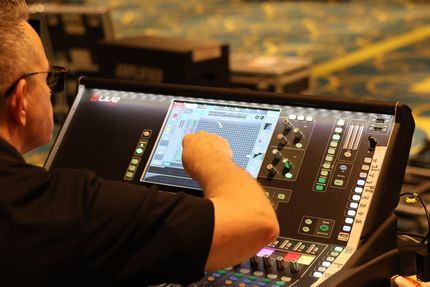 Person adjusting controls on a digital audio mixing console with a touchscreen in a dim studio.