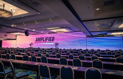 Empty conference hall with rows of chairs and a purple-blue “AMPLIFIED” stage backdrop