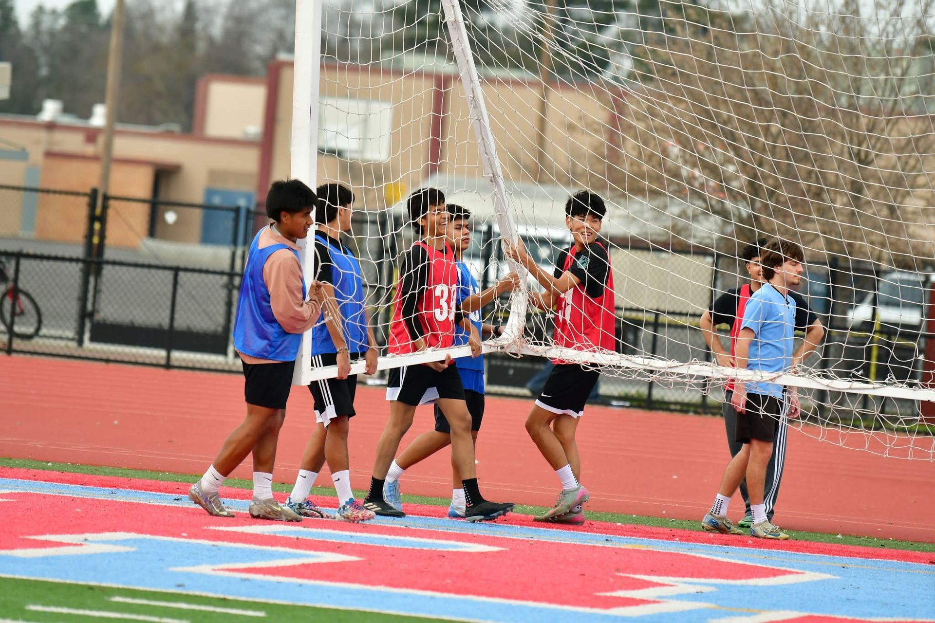 A group of athletes in practice jerseys move a soccer goal across a track field.
