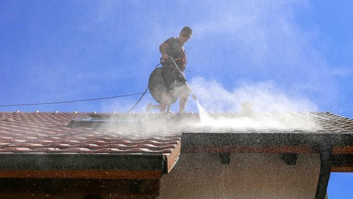 A man is cleaning the roof of a building with a high pressure washer.