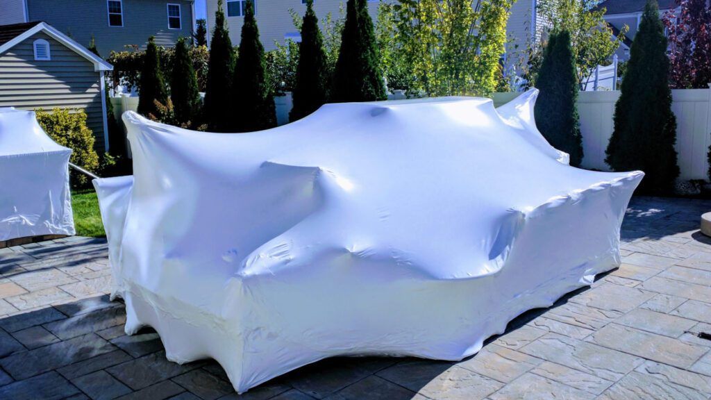 A couch is wrapped in white plastic wrap on a patio.