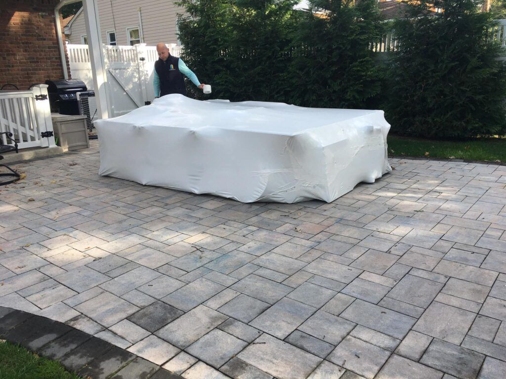A man is wrapping a large piece of furniture in plastic wrap on a patio.