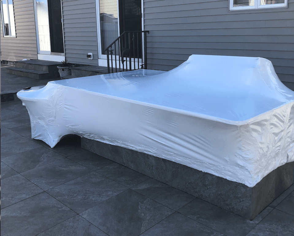 A pool is wrapped in plastic and sitting on a patio in front of a house.