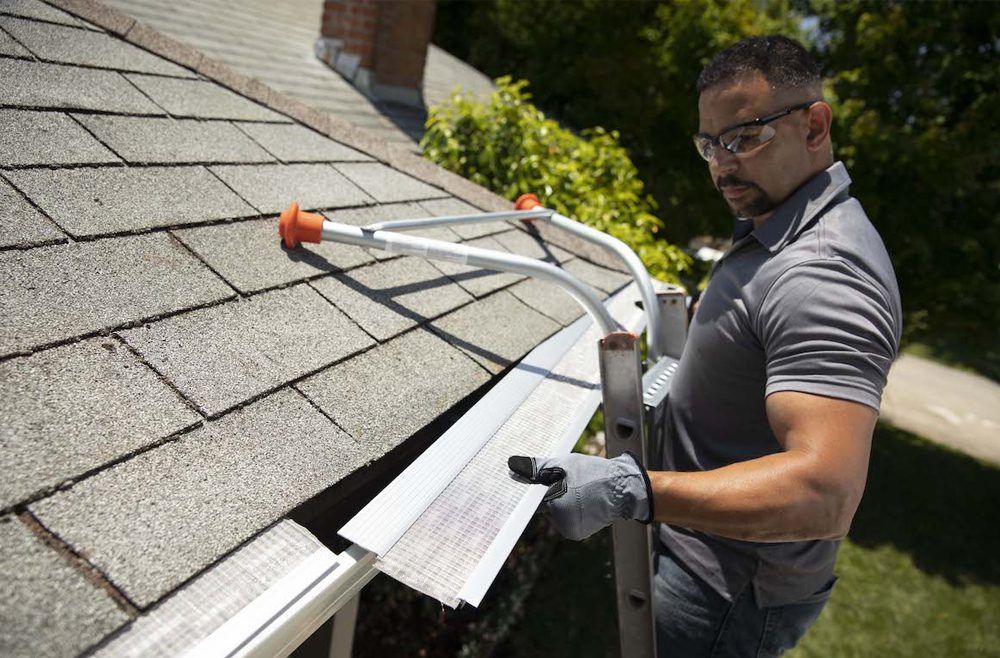 A man is standing on a ladder fixing a gutter on a roof.