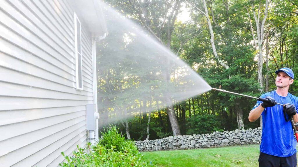 A man is using a high pressure washer to clean the side of a house.