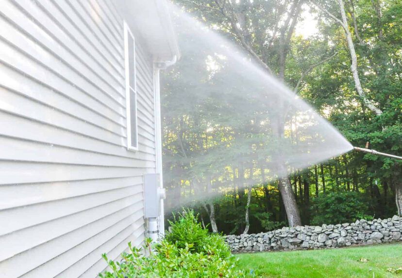 A man is using a high pressure washer to clean the side of a house.