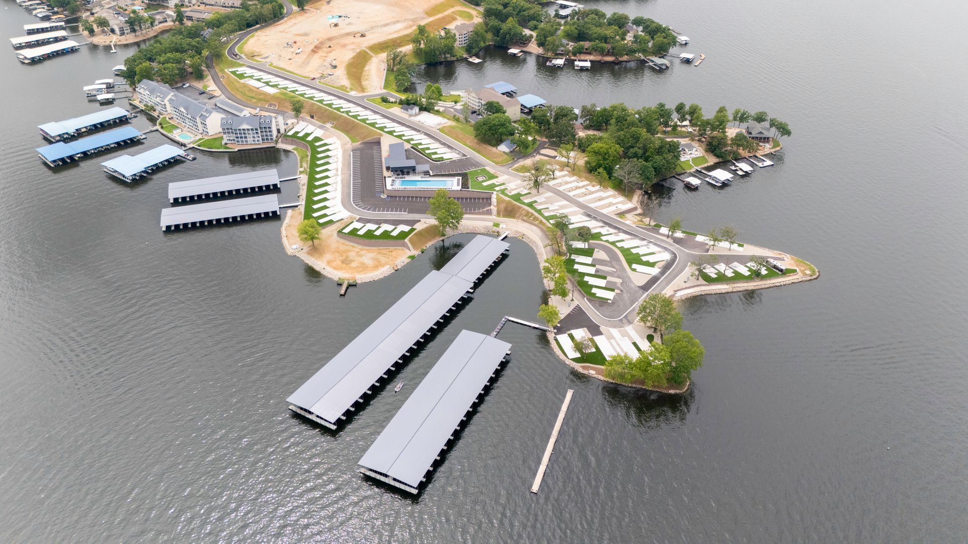 Aerial view of a lake with boat docks, a parking lot, and small buildings on a peninsula.