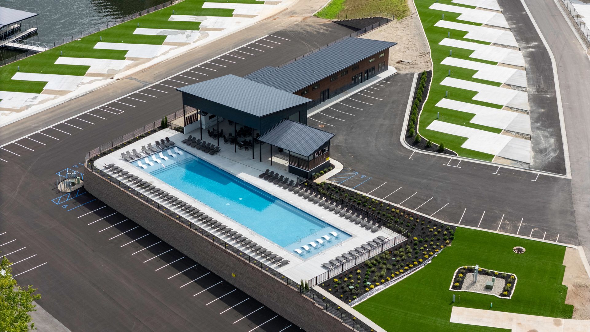 Swimming pool and clubhouse at an RV resort. Black asphalt, green grass, and clear blue water.