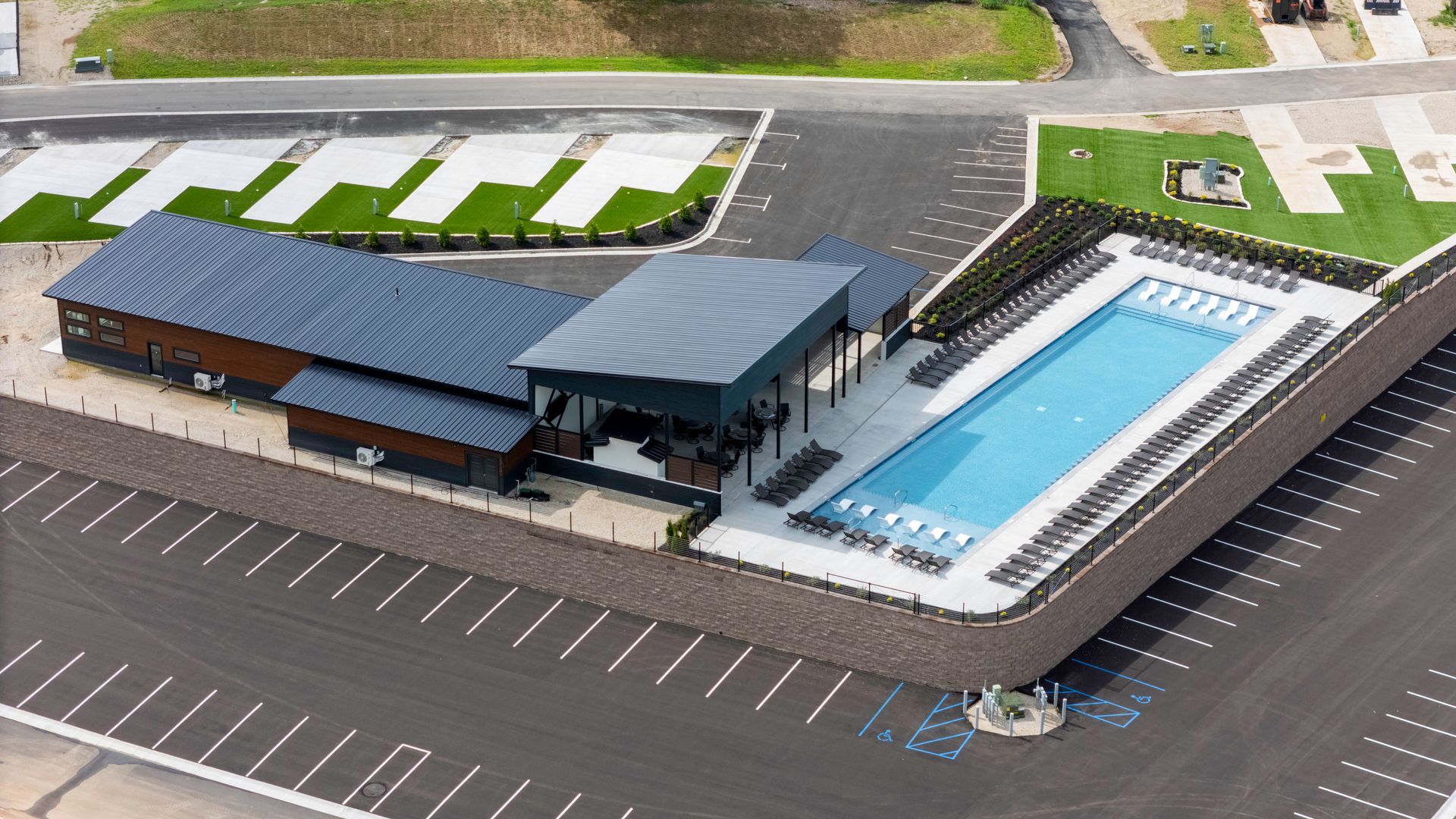 Aerial view of a modern building complex with a rectangular pool, parking, and green spaces.