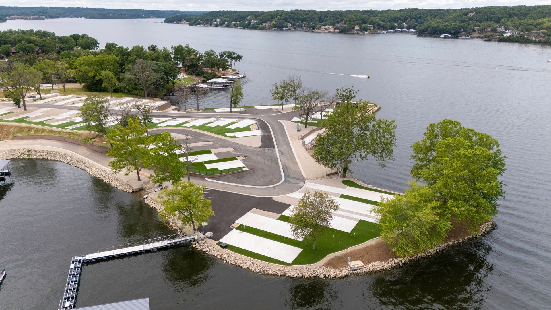 Aerial view of a lakeside RV park with campsites, trees, and a dock.