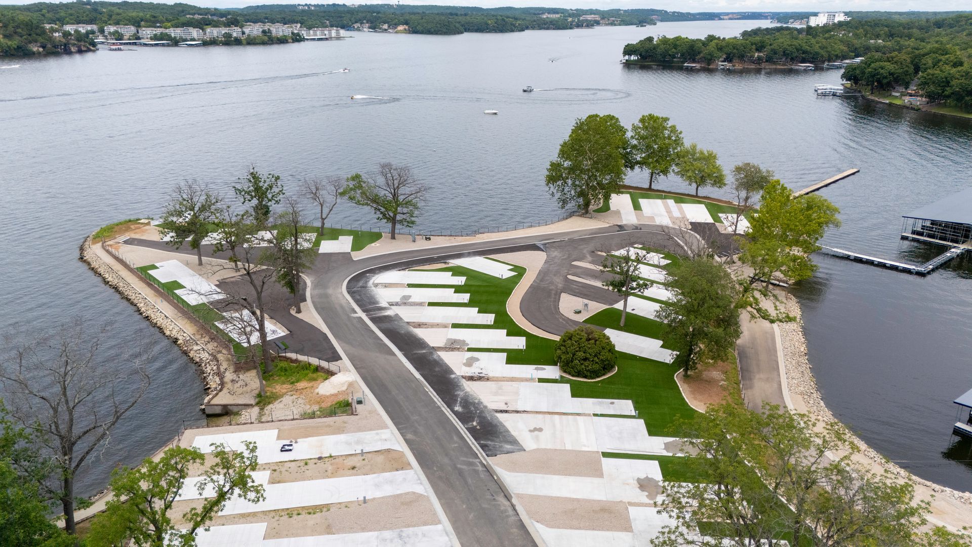 Aerial view of an RV park on a peninsula, with concrete pads, roads, and surrounding lake.