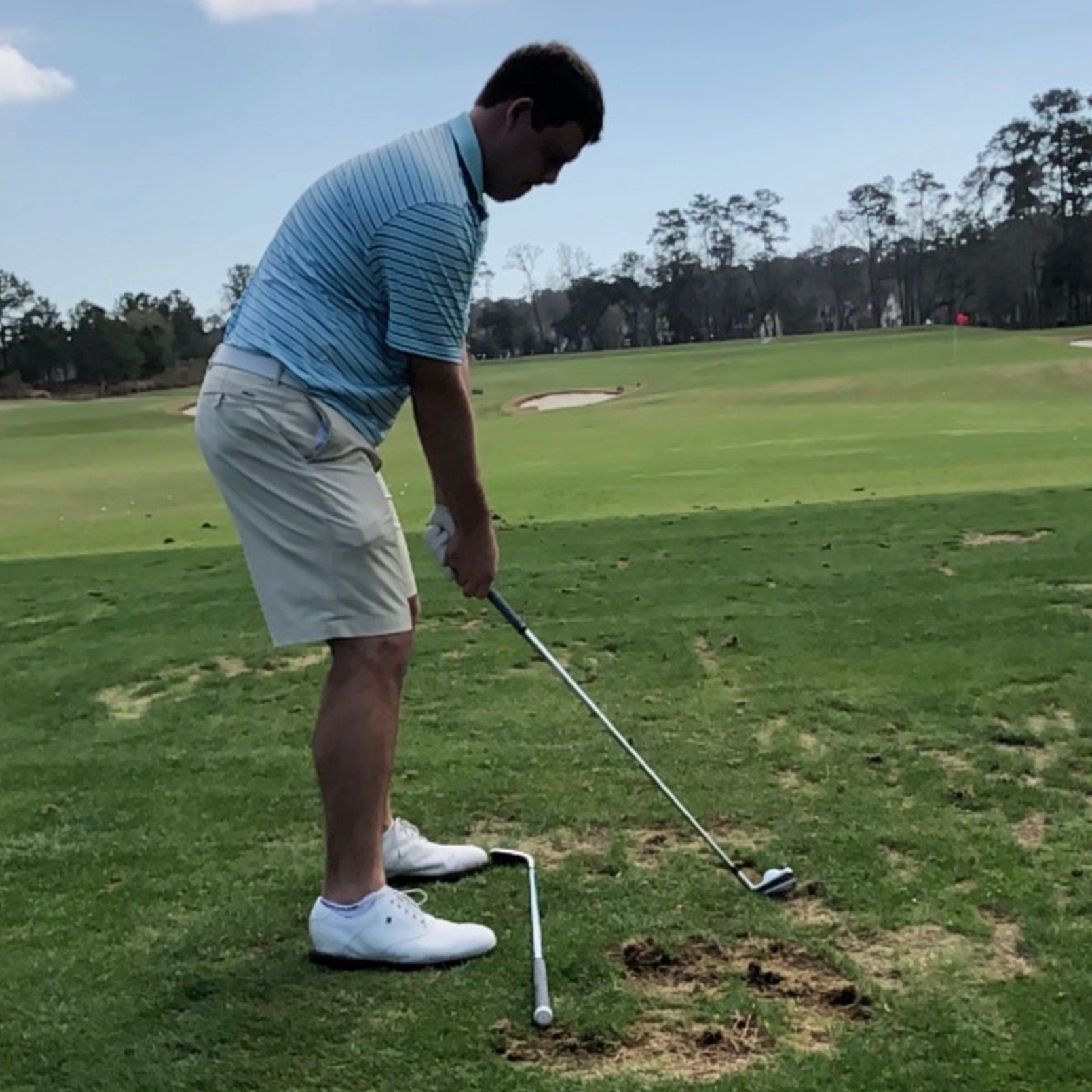 A man is swinging a golf club at a golf ball on a golf course.