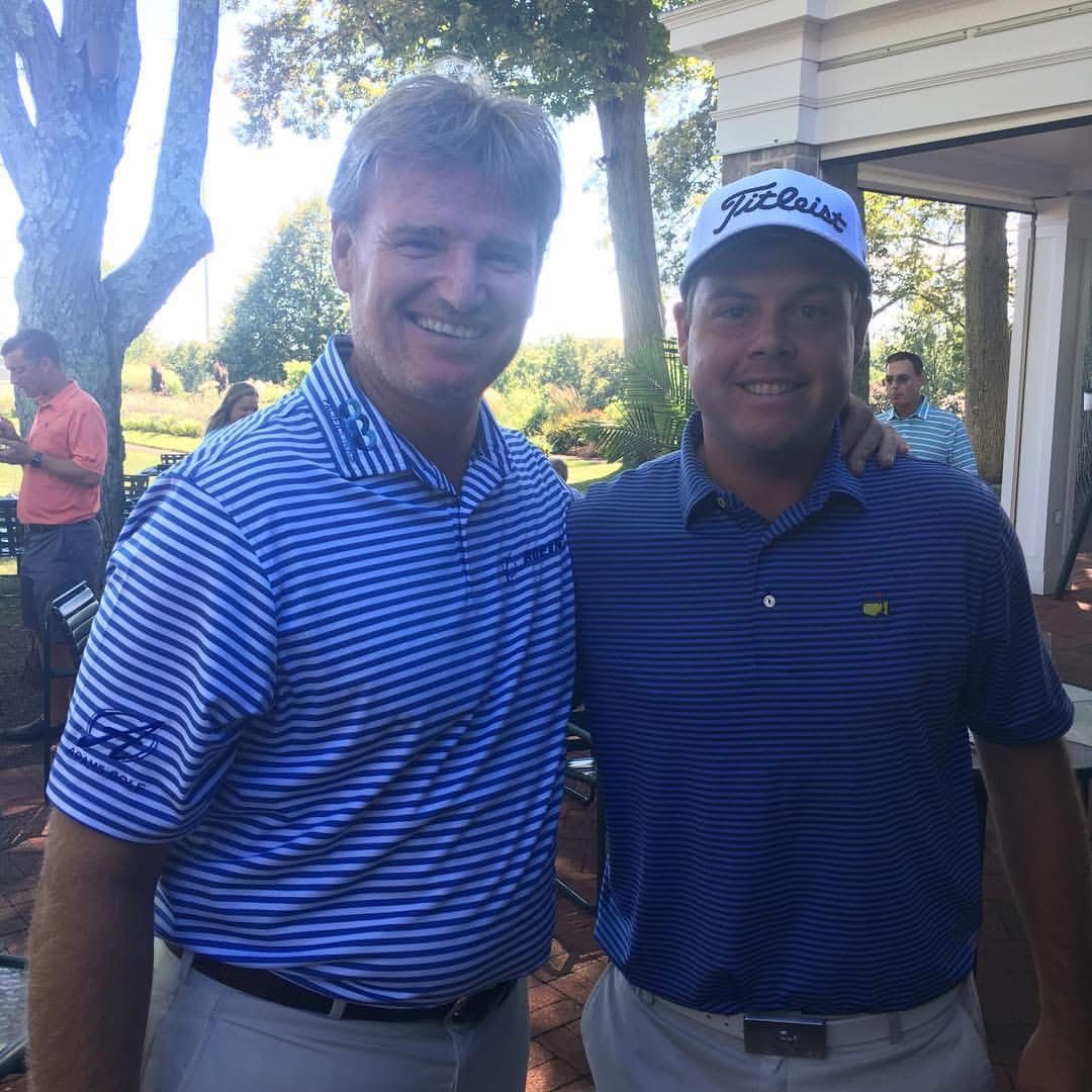 Three people are walking on a golf course with a golf cart in the background.