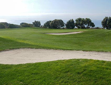 A golf course with a bunker in the middle of it and trees in the background.