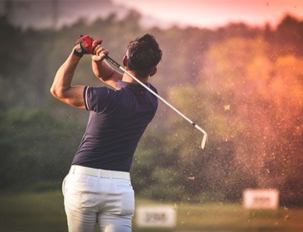 A man is swinging a golf club at a golf ball on a golf course.