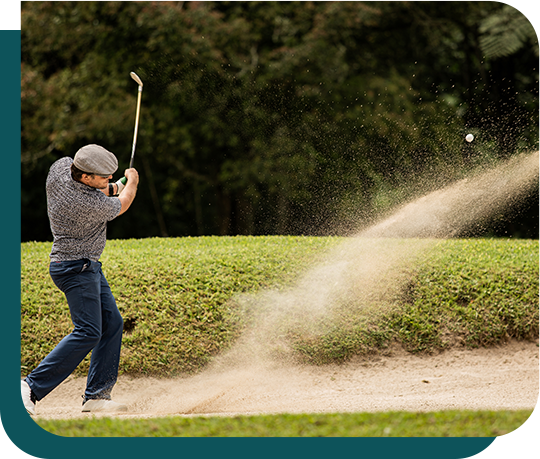A man is hitting a golf ball out of a bunker on a golf course.