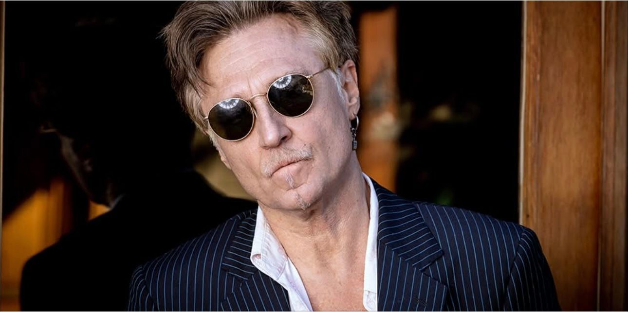 A man wearing sunglasses and a suit is standing in front of a door.