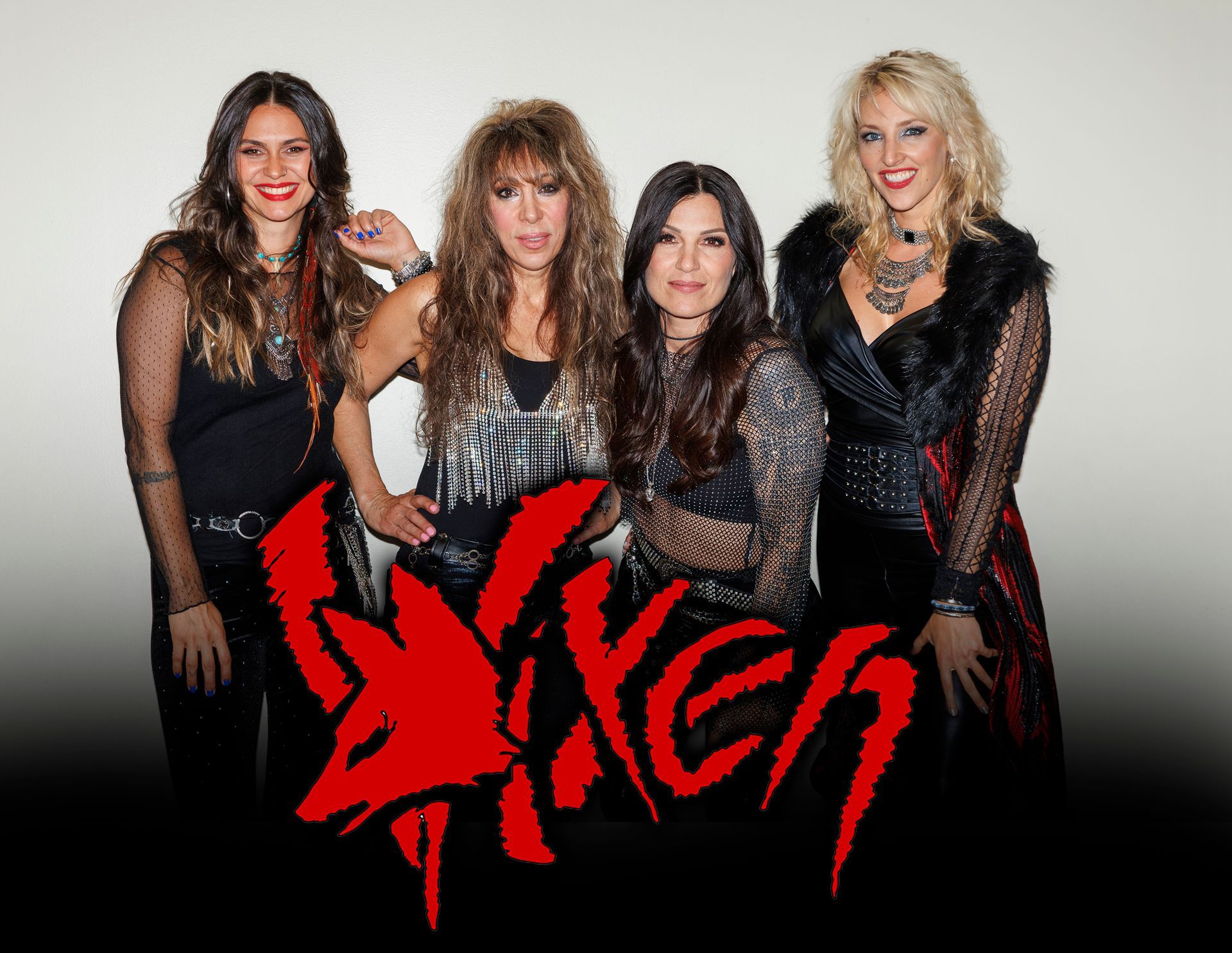 Ace Frehley, holding guitar, in sparkly jacket and pants. Lit stage background: red, blue, and purple.