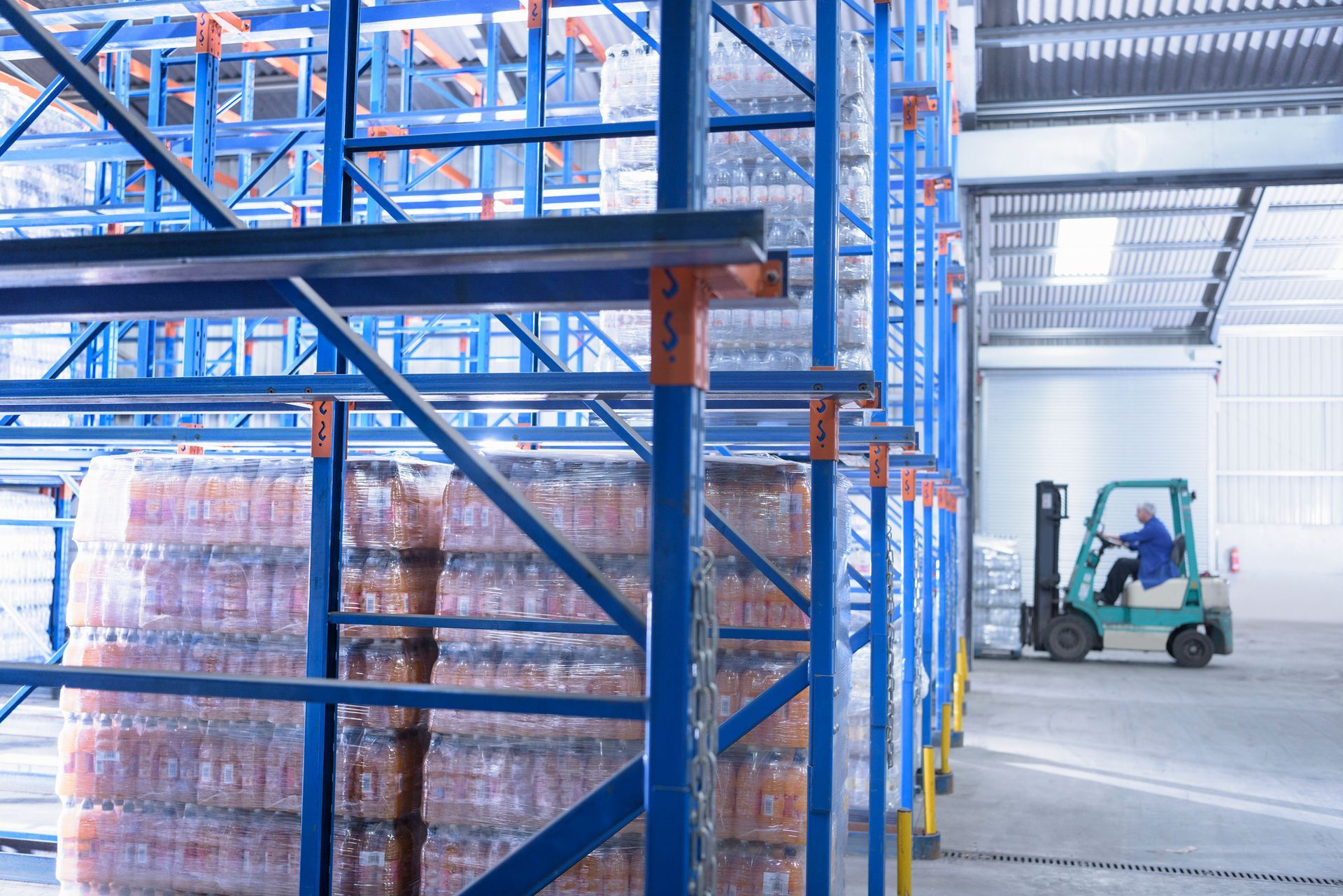 Yellow safety railings lead to a loading dock and closed gray door inside a warehouse. A yellow crane extends over the door.