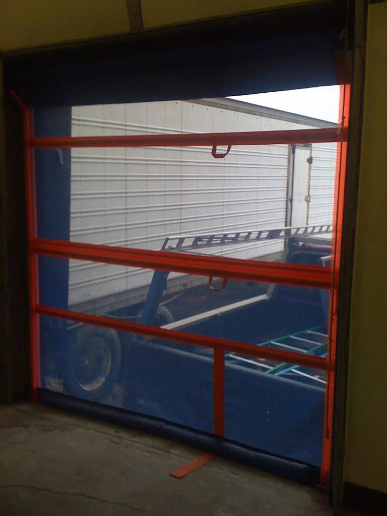 Mesh barrier with orange framing in an open doorway. Inside, a truck and loading equipment are visible.