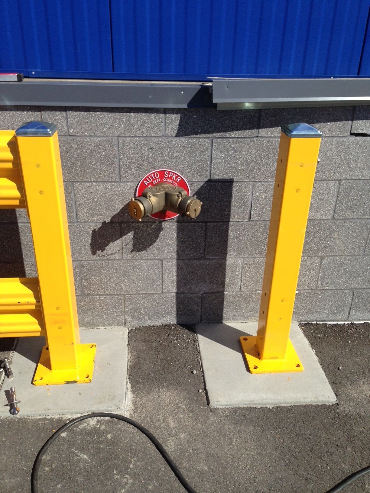 Yellow protective posts flank a fire hydrant on a brick wall, with blue corrugated metal above.
