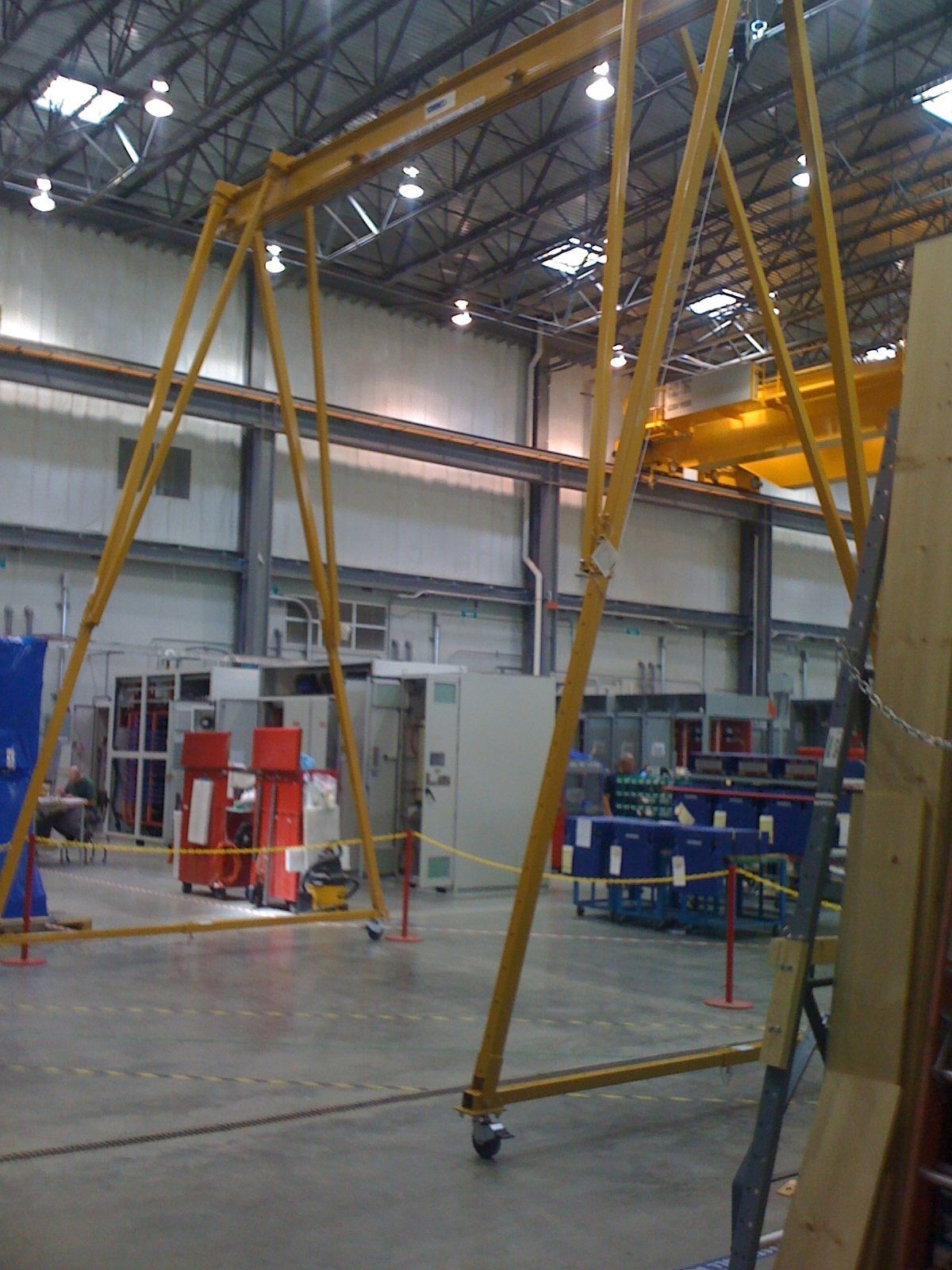 Yellow gantry crane on wheels in a warehouse. The crane is centered, with other equipment and machinery in the background.
