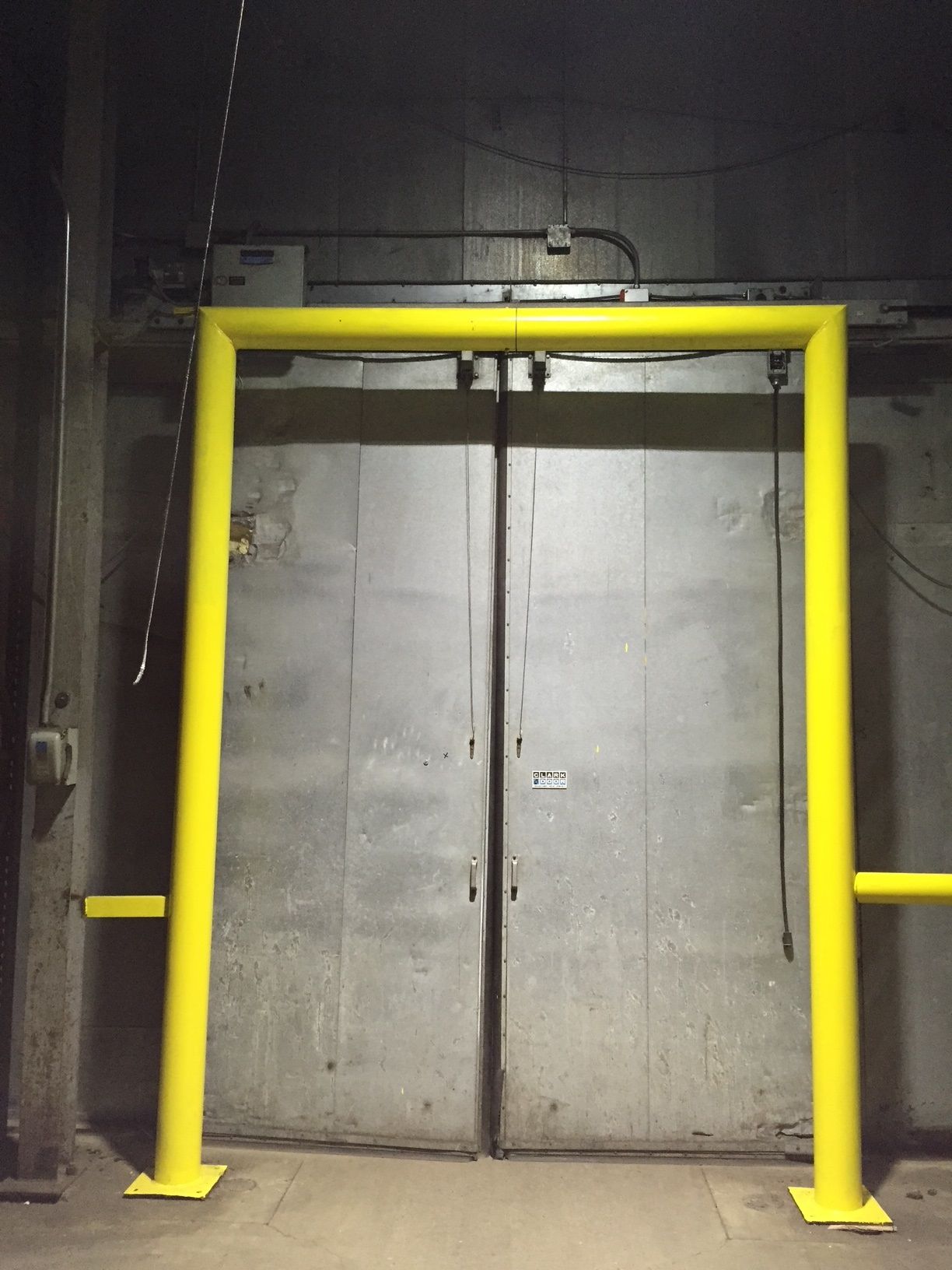Yellow safety gate surrounds a closed, gray metal door in an industrial setting.