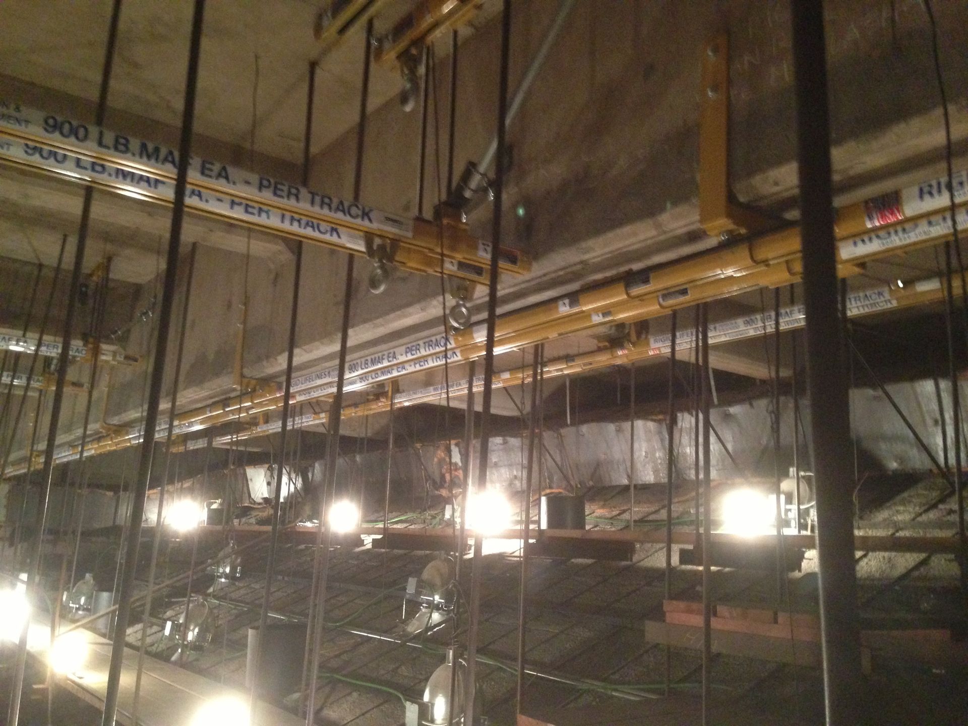 Interior construction scene: Yellow support tracks with labels, vertical metal supports, and work lights illuminating a dimly lit space.
