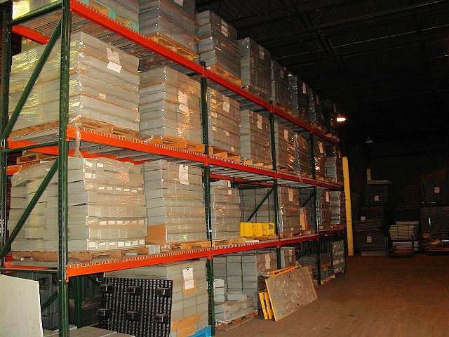 Warehouse shelves stacked with packaged goods; green shelves, orange beams, dark interior.