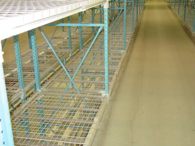 Warehouse shelving system with wire mesh decks, empty aisle, and concrete floor.
