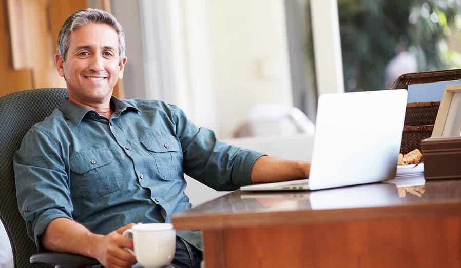 smiling man at laptop on desk with cup of coffee