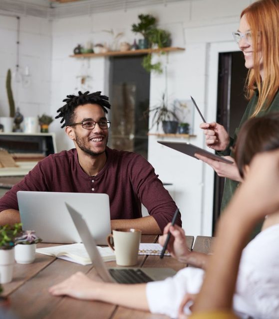 A group of people are sitting around a table with laptops.