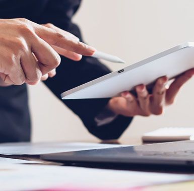 A person is holding a tablet and pointing at it with a pen.