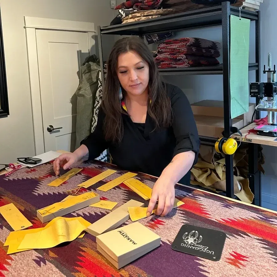 Woman arranging yellow leather pieces on a colorful fabric, near shelves and tools.