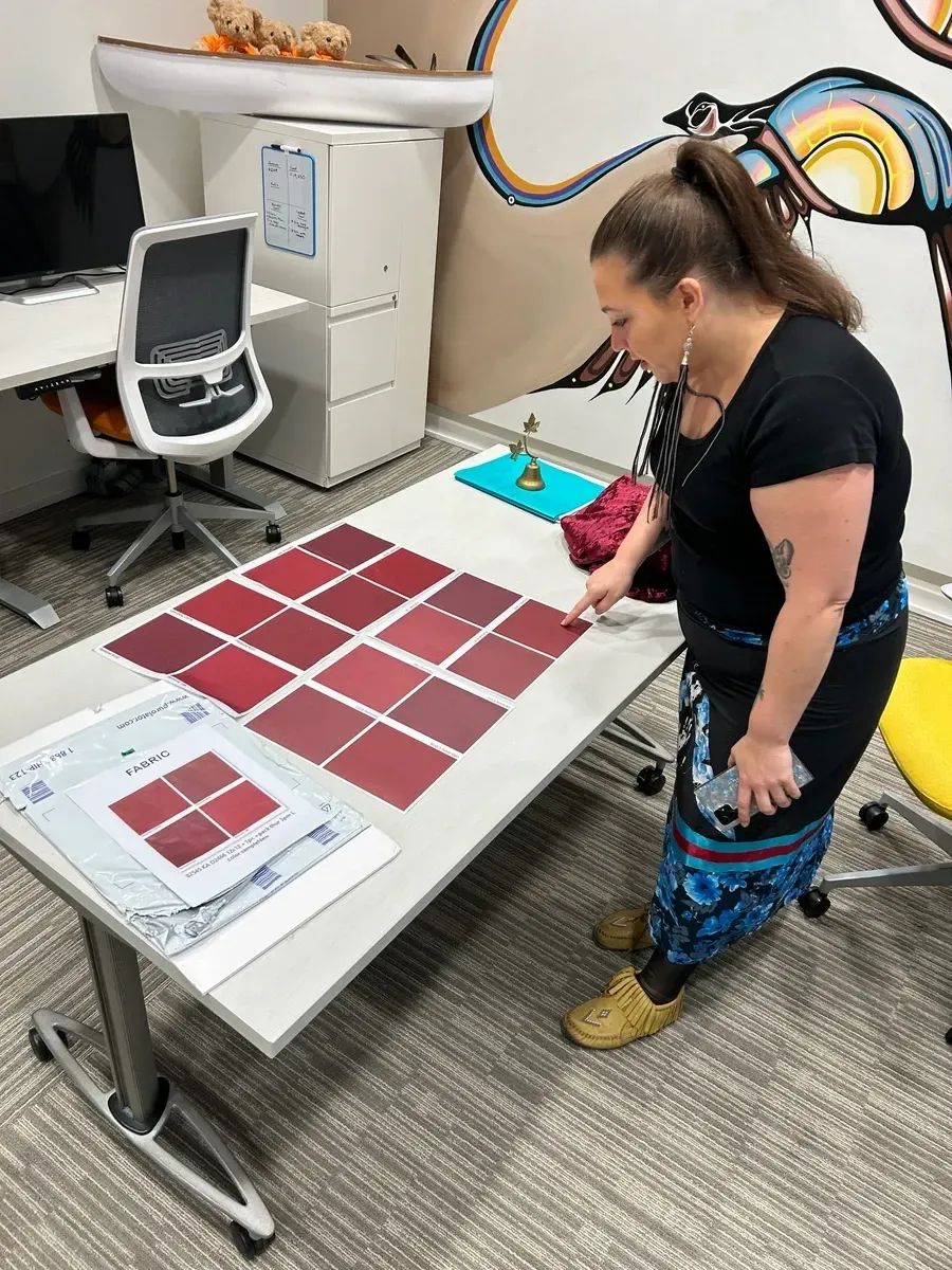 Woman pointing at red paint swatches on a desk. Office setting.